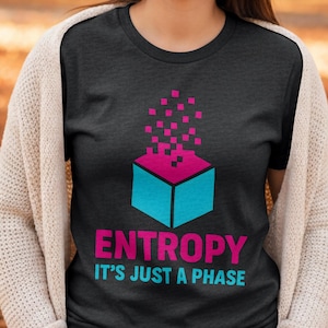 May include: Dark grey t-shirt with a geometric design of a blue and pink box and pink pixelated squares. The text "ENTROPY IT'S JUST A PHASE" is printed below the box in pink and blue.