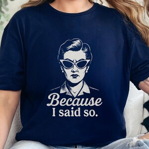 Op de afbeelding: Marineblauw T-shirt met een zwart-wit illustratie van een vrouw met een zonnebril. De tekst "Because I said so" is onder de illustratie gedrukt in een witte lettertype. Het T-shirt heeft een ronde hals.