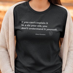 Op de afbeelding: Donkergrijs t-shirt met de quote "Als je het niet aan een zesjarige kunt uitleggen, begrijp je het zelf niet." van Albert Einstein. Het shirt heeft een ronde hals.