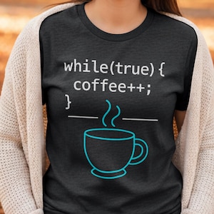 Op de afbeelding: Donkergrijs t-shirt met de tekst "while(true) { coffee++; }" in het wit. Daaronder een turquoise koffiekopje met stoom. Het t-shirt heeft een ronde hals.