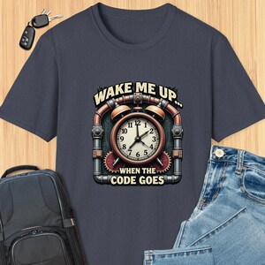 May include: A navy blue t-shirt with a steampunk-style clock design. The clock face reads "WAKE ME UP... WHEN THE CODE GOES".