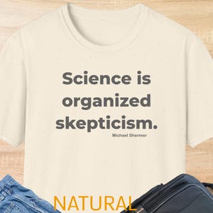 Puede incluir: Camiseta color crema con la cita "Science is organized skepticism" en texto gris, atribuida a Michael Shermer. La palabra "NATURAL" está impresa en amarillo en la parte inferior.