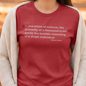 May include: A red t-shirt featuring the quote "In questions of science, the authority of a thousand is not worth the humble reasoning of a single individual." by Galileo Galilei. The shirt is worn with a cream cardigan.