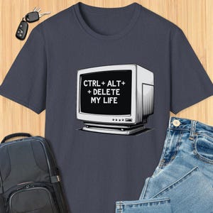 Può includere: Una maglietta blu navy con una grafica di monitor di computer retrò e il testo bianco "CTRL + ALT + DELETE MY LIFE". Il design è centrato sulla maglietta, realizzata in materiale morbido.