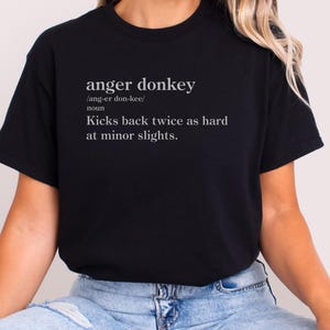 以下が含まれることがあります： 「anger donkey」の文字と発音記号がプリントされた黒いTシャツ。定義は「Kicks back twice as hard at minor slights.」クルーネックのTシャツです。
