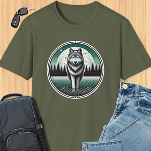 May include: A green t-shirt with a vintage-style graphic of a wolf standing in front of a full moon and trees. The graphic is in a circle with a distressed look.