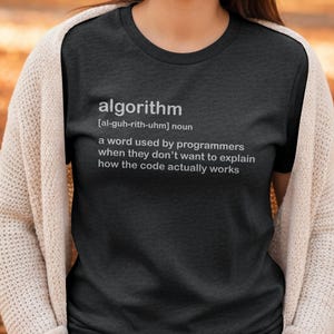 Op de afbeelding: Donkergrijs t-shirt met de definitie van "algoritme" in het wit gedrukt. De definitie luidt: "een woord dat door programmeurs wordt gebruikt als ze niet willen uitleggen hoe de code daadwerkelijk werkt."