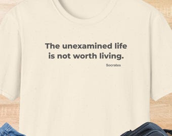 May include: Cream-colored t-shirt with the quote "The unexamined life is not worth living." in dark gray text. The quote is attributed to Socrates. The word "NATURAL" is printed in yellow at the bottom of the shirt.