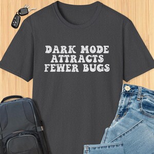 Pode incluir: Camiseta cinza escuro com um gráfico branco desbotado que diz "DARK MODE ATTRACTS FEWER BUGS".