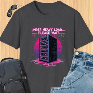 May include: A dark gray t-shirt with a retro-style graphic of a server rack with the text "Under Heavy Load... Please Wait."