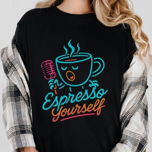 May include: Black t-shirt with a cartoon coffee cup design holding a microphone, steam, and the words "Espresso Yourself" in teal and orange. A fun, colourful graphic on a casual tee.