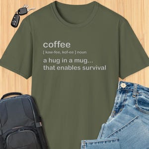 May include: Green t-shirt with a white graphic that says "coffee [kaw-fee, kof-ee] noun a hug in a mug... that enables survival"