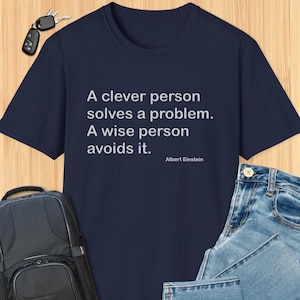 May include: A navy blue t-shirt with a white quote that reads "A clever person solves a problem. A wise person avoids it." The quote is attributed to Albert Einstein.