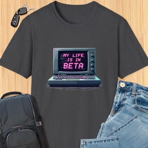 May include: A dark gray t-shirt with a retro computer graphic and the text "MY LIFE IS IN BETA" in pink neon letters.