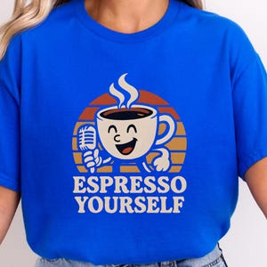Peut inclure: T-shirt bleu avec un dessin de tasse à café souriante tenant un microphone. La tasse est placée sur un fond circulaire marron et orange. Le texte "ESPRESSO YOURSELF" est imprimé en dessous.