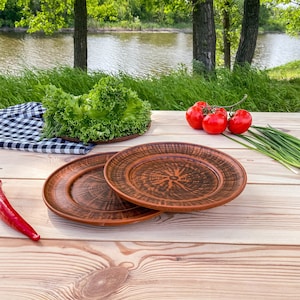 Puede incluir: Dos platos de cerámica marrón con un diseño decorativo se colocan sobre una mesa de madera. Una ensalada verde, tomates rojos y cebollas verdes están en el fondo.