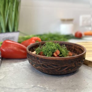 Peut inclure: Un bol en céramique brune avec un motif sculpté, rempli de tomates rouges hachées et d'aneth frais vert.