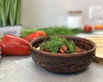 May include: A brown ceramic bowl with a carved design, filled with chopped red tomatoes and fresh green dill.
