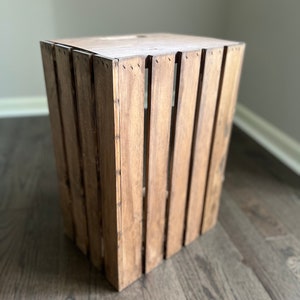 May include: A wooden crate with a natural brown finish. The crate is made of slats of wood and has a rectangular shape.