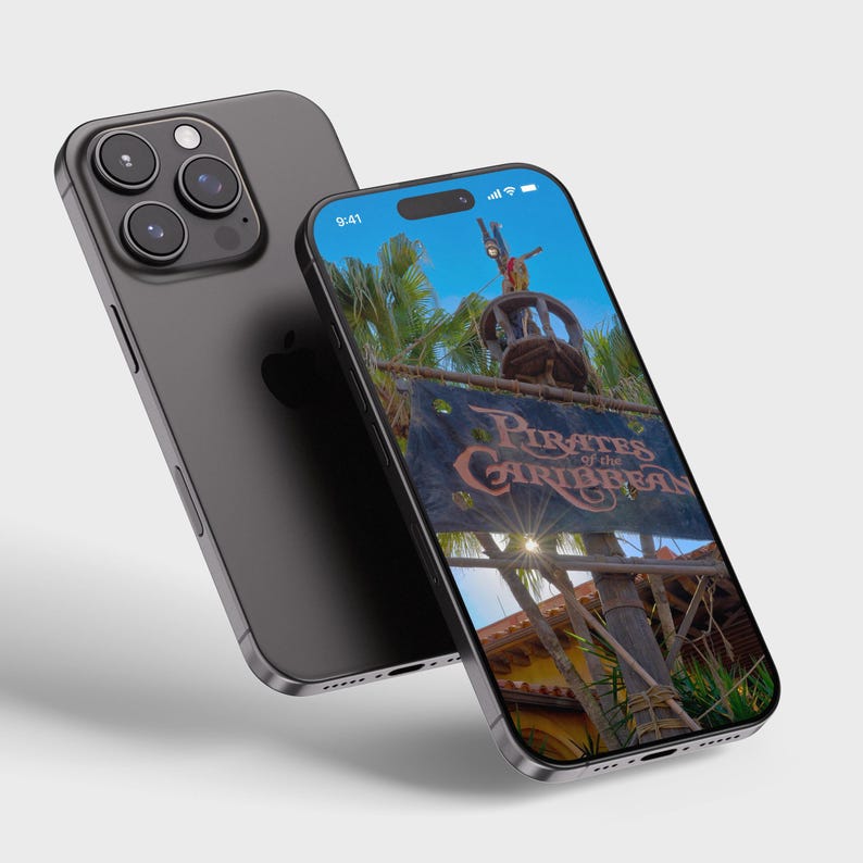 May include: A black iPhone with a screen displaying a photo of the Pirates of the Caribbean ride at a theme park. The screen shows a sign with the words "Pirates of the Caribbean" and a pirate ship in the background.