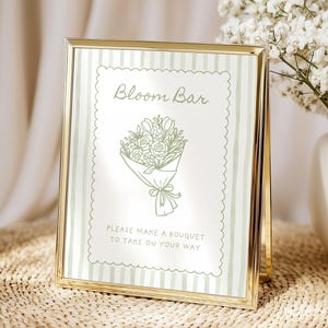 Puede incluir: Un letrero con marco dorado y fondo a rayas verdes y blancas. El letrero dice "Bloom Bar" encima de un dibujo de un ramo de flores. Debajo del dibujo, el letrero dice "Please make a bouquet to take on your way."