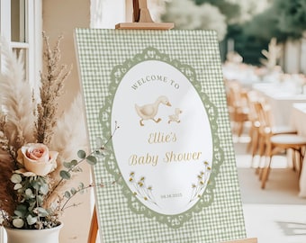 May include: A baby shower welcome sign on an easel. The sign has a green and white gingham background with an oval frame. Inside the frame is the text "Welcome to Ellie's Baby Shower" with a duck and duckling illustration. The date 08.18.2025 is also included.