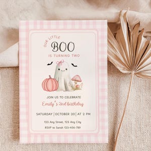 May include: A pink and white gingham-patterned invitation card with the text "Our Little Boo is Turning Two." The card features a cute ghost illustration, a pink pumpkin, and a mushroom. The text "Emily's 2nd birthday" is also included.