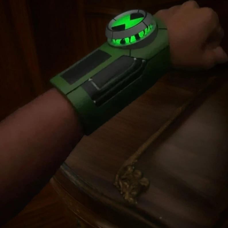 Peut inclure: Une montre-bracelet verte et noire avec un symbole vert lumineux au centre. La montre est con&ccedil;ue pour ressembler &agrave; l'Omnitrix de la s&eacute;rie anim&eacute;e Ben 10.