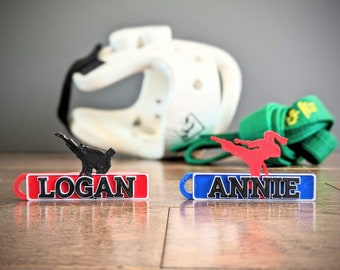 May include: Two personalized red and blue keychains with black text. Each keychain features a silhouette of a person in a martial arts pose. The keychain on the left says "LOGAN" and the keychain on the right says "ANNIE".