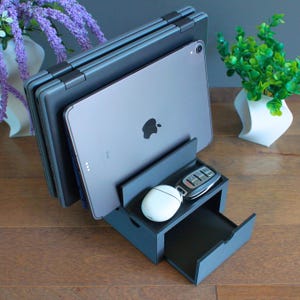 May include: A black desktop organizer with a drawer, a compartment for a tablet or phone, and a space for keys. The organizer is holding a tablet, a phone, and a set of keys.