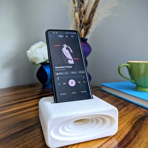 Phone stand with acoustic booster. Comes in a variety of colors and may be customized for the dimensions of any device.