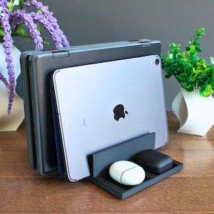 May include: A black stand with a grey iPad and two white wireless earbuds. The stand is on a wooden surface.