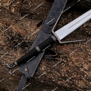 May include: A silver sword with a black handle and a leather scabbard. The sword has a curved blade and a decorative handle.