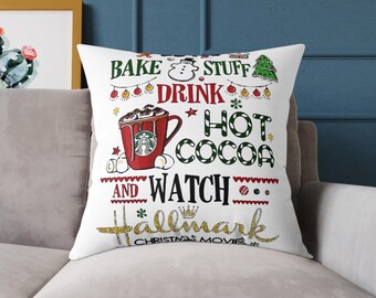 May include: White decorative pillow with a festive Christmas design. The pillow features text that reads "Bake Stuff, Drink Hot Cocoa, and Watch Hallmark Christmas Movies" with a red mug, snowman, and Christmas tree.