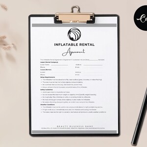 May include: A black clipboard holds an "Inflatable Rental Agreement" form with a logo and text. A black pen rests on a light brown surface. The agreement includes sections for the lessor, lessee, setup requirements, safety guidelines, and weather conditions.