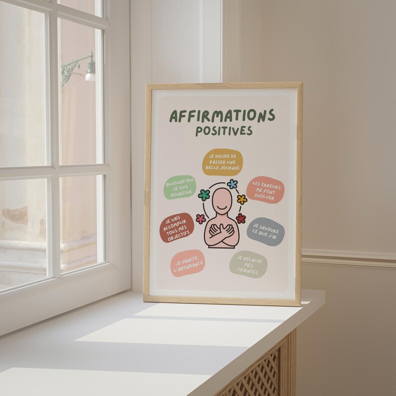 May include: A framed print with the words "AFFIRMATIONS POSITIVES" in green. The print features a cartoon figure with arms crossed, surrounded by colorful text bubbles with positive affirmations in French. The frame is light brown.