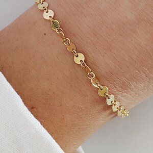 May include: A gold chain bracelet with small round links. The bracelet is on a person's wrist.
