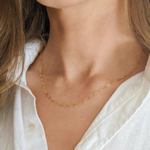 May include: A delicate gold necklace featuring a repeating heart design. The necklace is worn against a white collared shirt. The chain is thin and the hearts are small and evenly spaced.