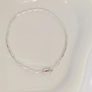 Puede incluir: Un brazalete de cadena de plata con cierre de langosta.