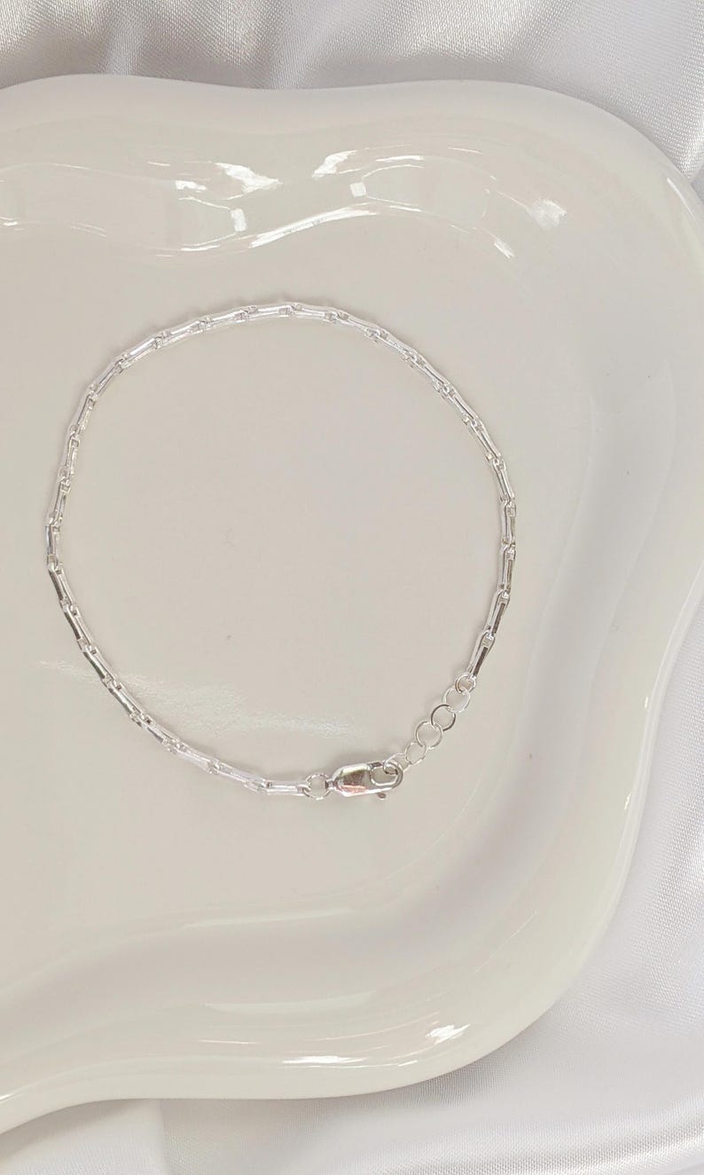Puede incluir: Un brazalete de cadena de plata con cierre de langosta.