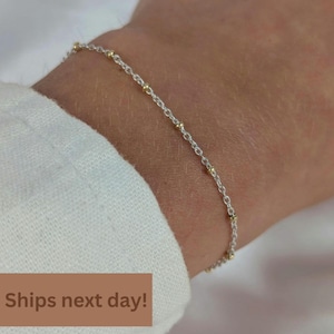 May include: A delicate chain bracelet featuring a silver-toned link design interspersed with small, evenly spaced gold-toned beads. The bracelet rests against the skin, showcasing a minimalist aesthetic with alternating metallic elements throughout the chain.