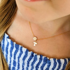 May include: A gold chain necklace with a small white daisy charm and a gold letter "T" charm.