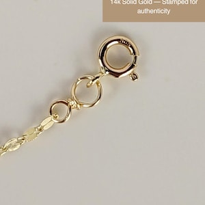 May include: Close-up of a 14k solid gold necklace clasp and chain. The clasp is round with a small lever, and the chain has a delicate, flat link design. Text reads: "14k Solid Gold &mdash; Stamped for authenticity."