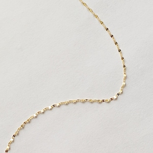 May include: A delicate gold-colored necklace with a repeating oval link chain design. The chain is displayed against a white background, highlighting its subtle shine and intricate pattern. This piece is suitable for everyday wear.