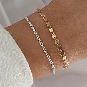 Puede incluir: Dos pulseras en una mu&ntilde;eca. Una pulsera es plateada y tiene un dise&ntilde;o de cadena de eslabones. La otra pulsera es dorada y tiene un dise&ntilde;o de cadena de eslabones con eslabones redondos y planos.