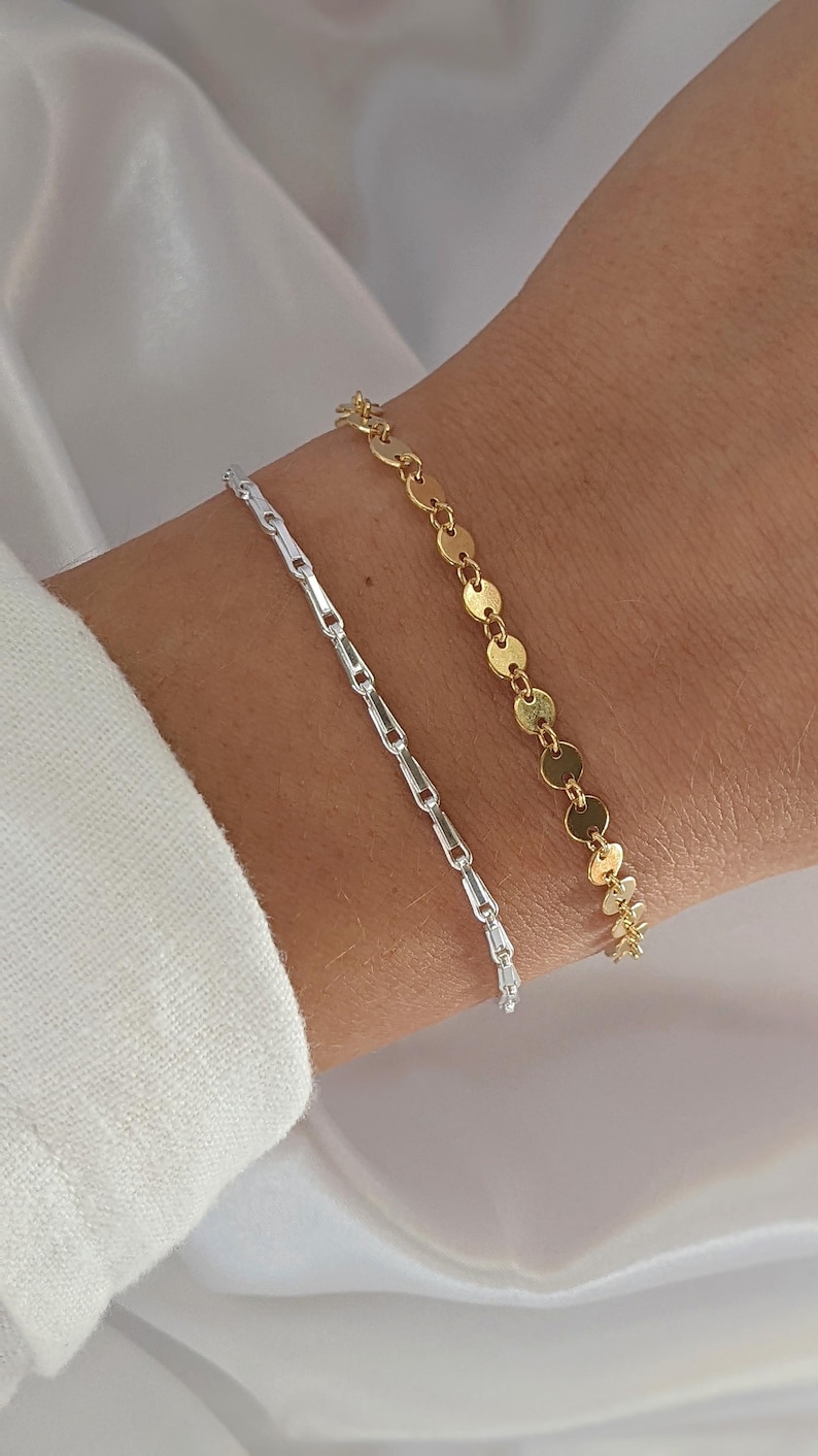 Puede incluir: Dos pulseras en una mu&ntilde;eca. Una pulsera es plateada y tiene un dise&ntilde;o de cadena de eslabones. La otra pulsera es dorada y tiene un dise&ntilde;o de cadena de eslabones con eslabones redondos y planos.