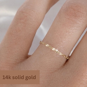 May include: A delicate 14k solid gold ring with a chain-like design. The ring is thin and features a repeating pattern of small, leaf-shaped links. The ring is shown on a finger, with the text "14k solid gold" in a brown box.