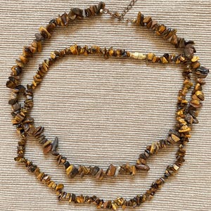 Peut inclure: Un collier à double rang composé d'éclats de pierre œil-de-tigre irréguliers et polis dans des tons brun doré et brun foncé. Le collier est doté d'un fermoir métallique et d'une chaînette d'extension réglable pour un ajustement personnalisé.