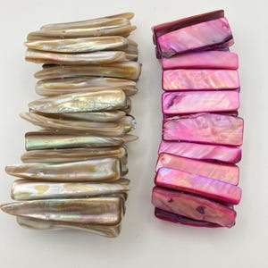 Op de afbeelding: Twee elastische armbanden gemaakt van rechthoekige schelpsegmenten. De ene armband heeft iriserende, lichtbruine en beige schelpstukjes met een natuurlijke glans. De tweede armband bestaat uit levendige, gepolijste felroze schelpsegmenten.