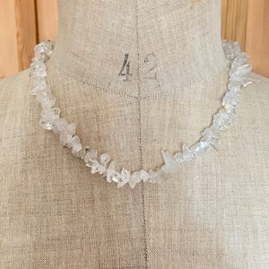 Peut inclure: Un collier composé de nombreuses petites pépites de cristal transparentes et translucides, aux formes irrégulières. Les pierres présentent une texture brute et dentelée, variant en taille et en forme pour former une bande continue et texturée.